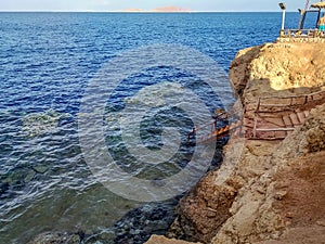 Seascape in Sharm El Sheikh Egypt and Tiran Island on the horizon. An old rusty metal staircase descends from a cliff to a coral