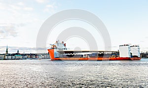 Seascape side view of a large orange semi-submersible heavy-lift ship with large load entering harbor in Stockholm Sweden.
