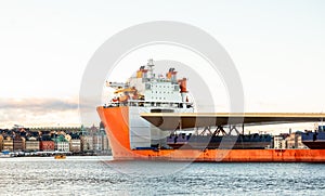 Seascape side view of a large orange semi-submersible heavy-lift ship with large load entering harbor in Stockholm Sweden.