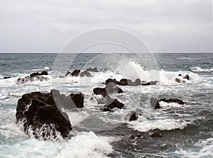 Seascape with stormy dramatic waves breaking over coastal rocks with white surf