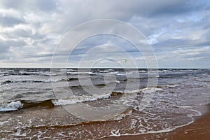 Seascape in summer with kitesurfers and green sails. Cloudy dramatic skies and waves washing the beach