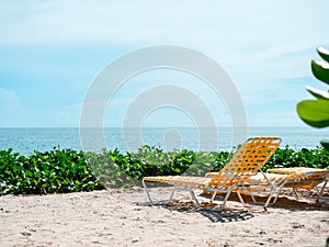 Seascape. Summer view with orange sunbeds with nobody on the beach sand on blue sky background on sunny day.