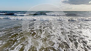 Seascape on a sunny summer day. Huge waves roll onto the shore, creating white foam. Slow motion