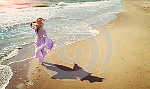 A young happy woman walks carelessly along the seashore in a pink flowing photo