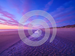 Seascape during sunrise. Bright clouds on the sky. Lines of sand on the seashore. Bright sky during sunset.