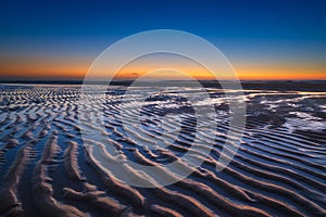 A seascape during sunset. Lines of sand on the seashore. Bright sky during sunset. A sandy beach at low tide.