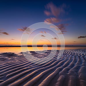 A seascape during sunset. Lines of sand on the seashore. Bright sky during sunset. A sandy beach at low tide.