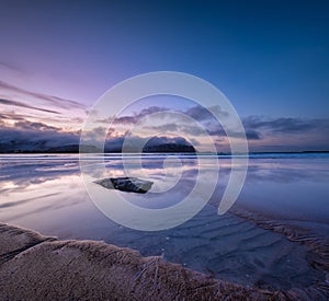 A seascape during sunset in Lofoten islands, Norway. Sand on the seashore. Bright sky during sunset. A sandy beach at low tide. Lo