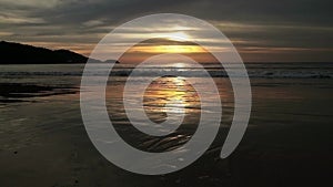 Seascape at sunset reflected on wet beach sand with incoming waves