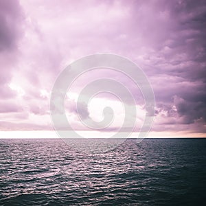 Seascape tinted in purple color picture. The sky with clouds, waves on the sea surface, dark toning abstract photo