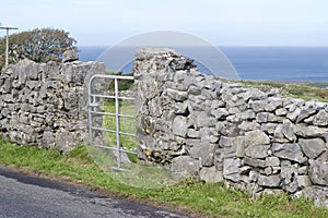 Seascape view of a gate and stone wall along a road on the rugged terrain of Inishmore island in Ireland