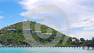 Seascape view of resort or village with solar cell rooftop on green mountain and blue sky with clouds background in summertime.