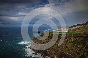 Seascape view with rocky cliffs after rain, a rainbow on a cloudy sky