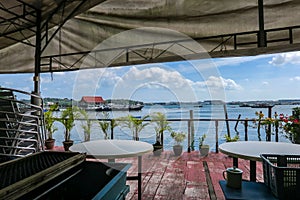 Seascape view of Singapore Straits and Pulau Ubin Jetty from wooden terrace with palm trees and tables on Pulau Ubin Island