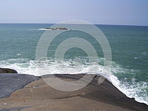 Seascape of white foamy water splashing on rocks at greenish blue sea