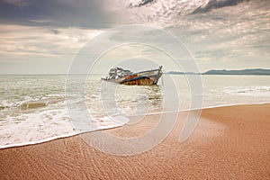 seascape of wreck boat on sand beach with cloudy sky in tropical region season