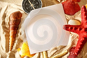 Seashells, compass and paper on sand