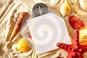 Seashells, compass and paper on sand