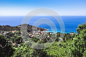 Seashore coastline with beach and rocks and rocky slope of the Island of Elba in Italy. Many people on the beach sunbathing. Blue