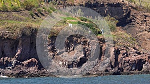 Seashore of Lipari Island. Mountain with green trees, vineyard and small cemetery. Mediterranean sea. Summer sunny day