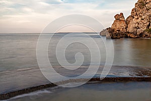 Seashore with rocks and pier, blurred water movement in evening