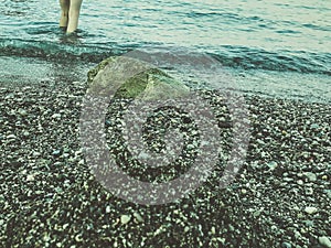 Seashore with water and sand. a girl in protective slippers walks along the stones near the shore. tidal bore. wet stones. waves