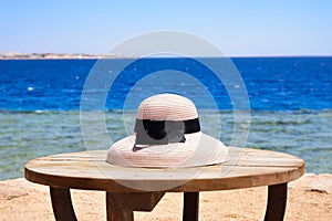 Seaside abstract, lady's light pink hat (bell-shaped) on the round table in front of deep blue sea water