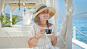 At a seaside cafe young brunette woman drinks her coffee looking the sea waves. Essence of summer holidays, vacation