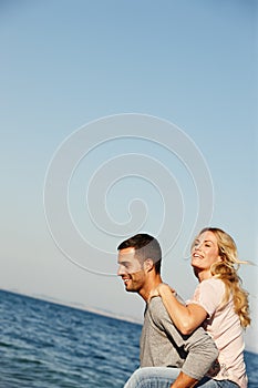 Seaside fun and romance. a young man giving his girlfriend a piggyback by the sea.