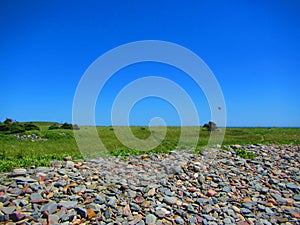 Seaside meadow with rock pile and kiteboarder in the distance