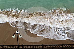 sea promenade with lantern and sand beach in stormy weather with waves