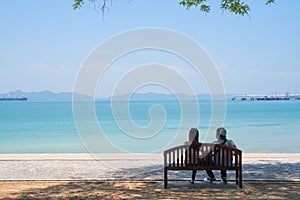 At seaside in summer , happy young couple in love relaxing on beach vacation enjoying ocean view together sitting on wooden chair