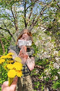 Season allergy to flowering plants pollen. Young woman with paper handkerchief covering her nose in garden and doing stop sign to