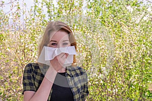 Season allergy to flowering plants pollen. Young woman with paper handkerchief in hand covering her nose in garden. Teen