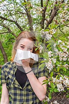 Season allergy to flowering plants pollen. Young woman with paper handkerchief in hand covering her nose in garden. Teen