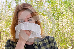 Season allergy to flowering plants pollen. Young woman with paper handkerchief in hand covering her nose in garden. Teen girl