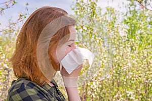 Season allergy to flowering plants pollen. Young woman with paper handkerchief in hand covering her nose in garden. Teen girl