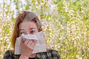 Season allergy to flowering plants pollen. Young woman with paper handkerchief in hand covering her nose in garden. Teen girl