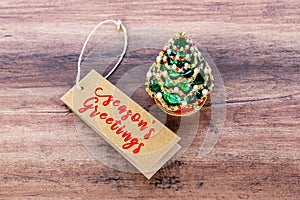 Season`s Greetings with mini Christmas tree on wooden background