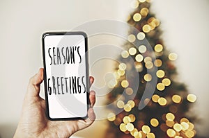 Season`s greetings text on phone screen on background of golden