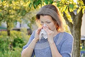 Seasonal allergies, woman with nasal wipe, sneezing, wiping nose outdoor