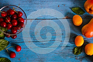 seasonal apricots pear and cherry in a glass bowl on a blue wooden background