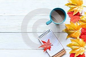 Seasonal autumn maple leaves.  Cup coffee hot steaming  warm scarf with paper note for greeting text on wooden table