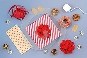 Seasonal christmas flat lay with red and white triped gift box with big ribbon, gift wrapping material, pine cones