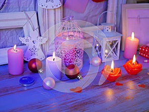 Seasonal festive interior composition of balls, lit candles, wooden frames, decorative lamps, felt hearts, paper for notes on a wo