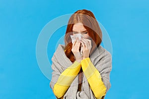 Seasonal flu. Cute redhead female student cought cold, sneezing in napkin, wear sweater and scarf on shoulders, feeling
