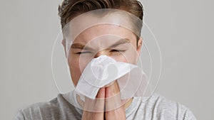 Seasonal flu. Young man suffering from runny nose, blowing into tissue, slow motion