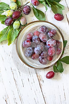 Seasonal food background. Ripe juicy plums in a bowl on a rustic wooden table. Top view flat lay. Copy space.