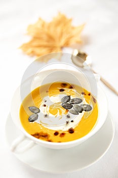 Seasonal food.Pumpkin soups. Soup decorated with cream sauce and pumpkin seeds. White background .Autumn foliage.Autumn.