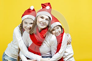 Seasonal Holidays Ideas. Three Happy Caucasian Family Girls In Santa Hats Having Fun While Embracing With Each Other And Hugs Over